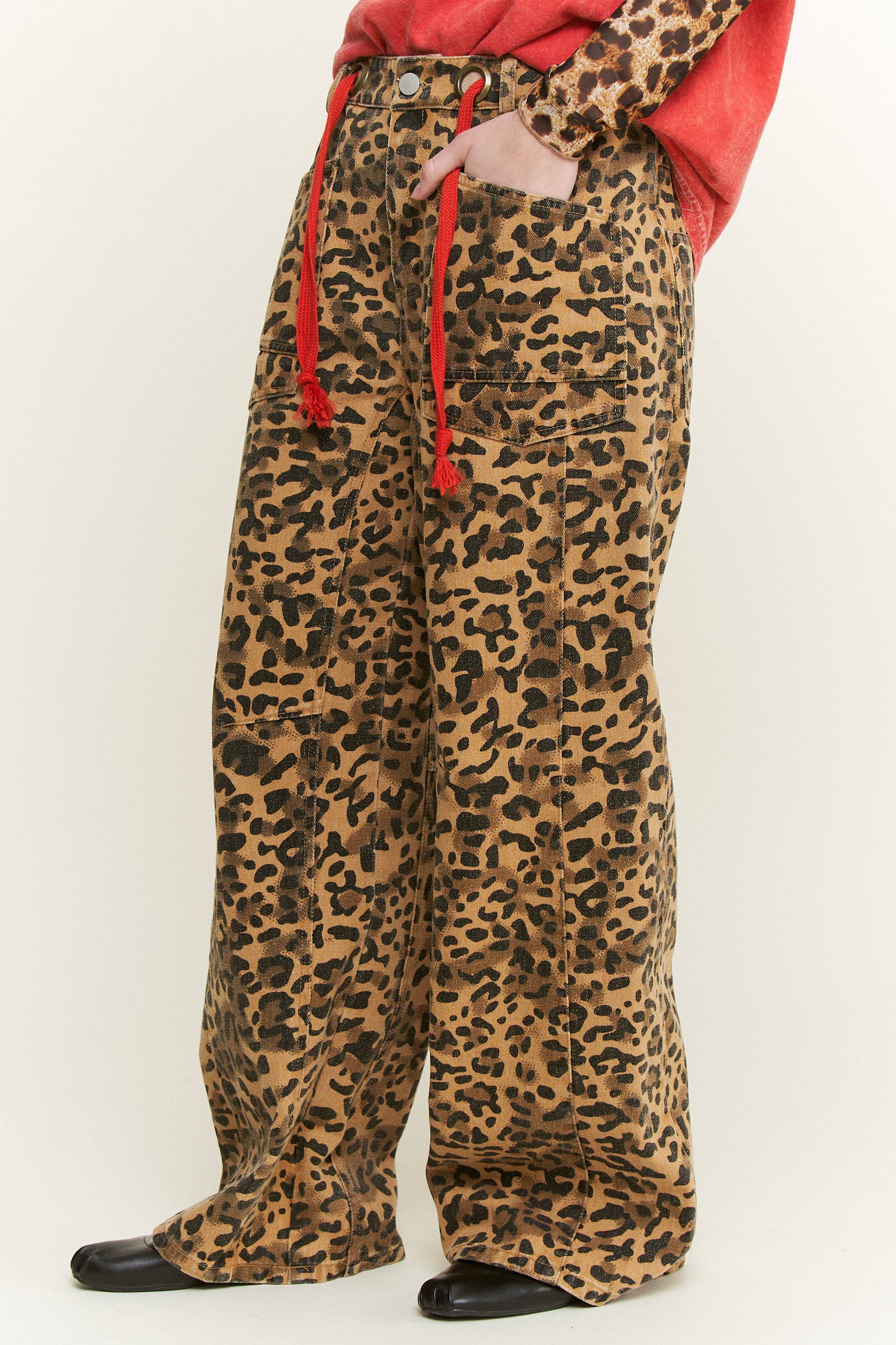 Full-length side view of leopard-print wide-leg pants with front patch pockets and red rope belt tips.