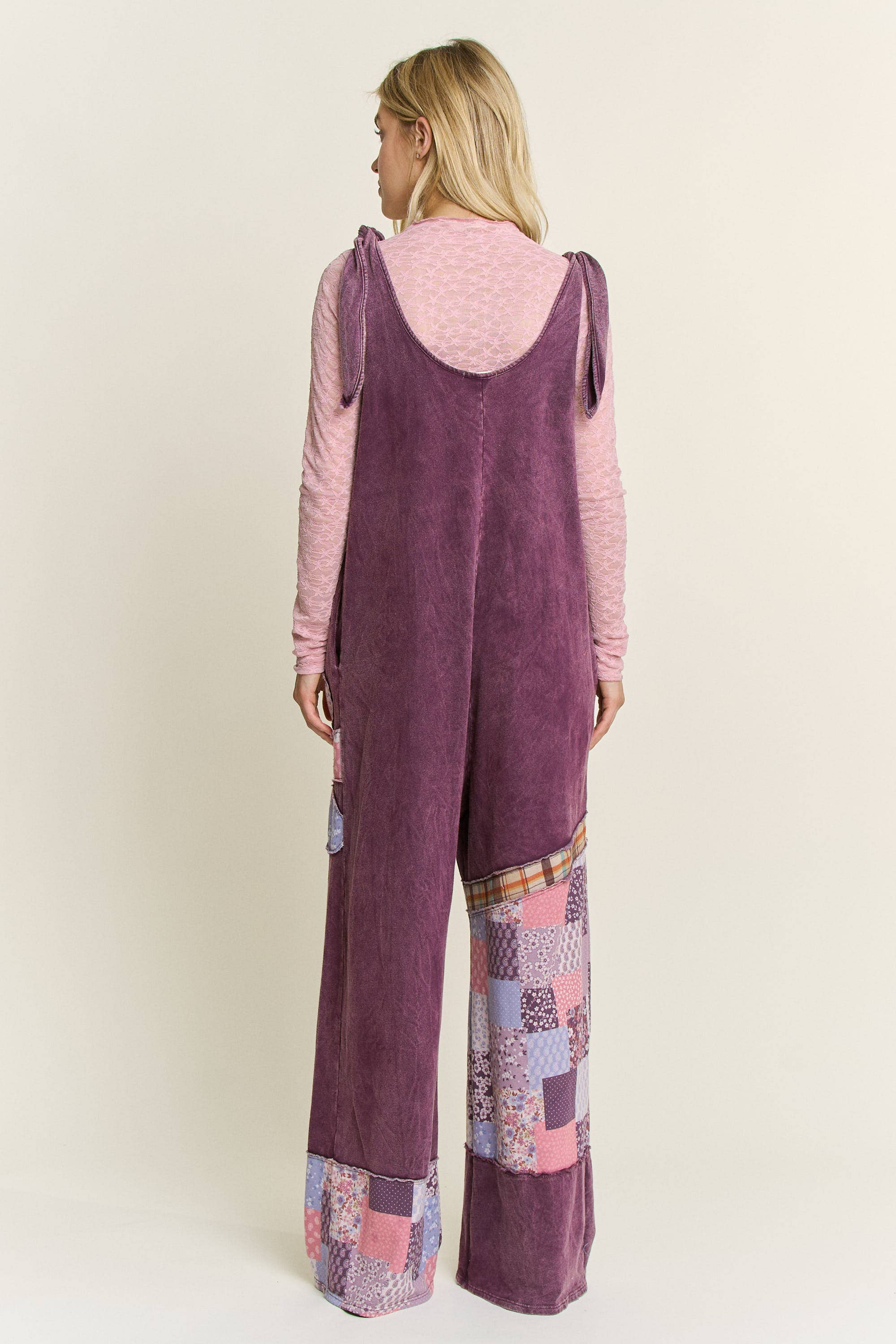 Rear view of a person wearing a eggplant patchwork mineral wash jumpsuit . boho patchwork mineral-wash jumpsuit with daisy appliqués and wide legs.