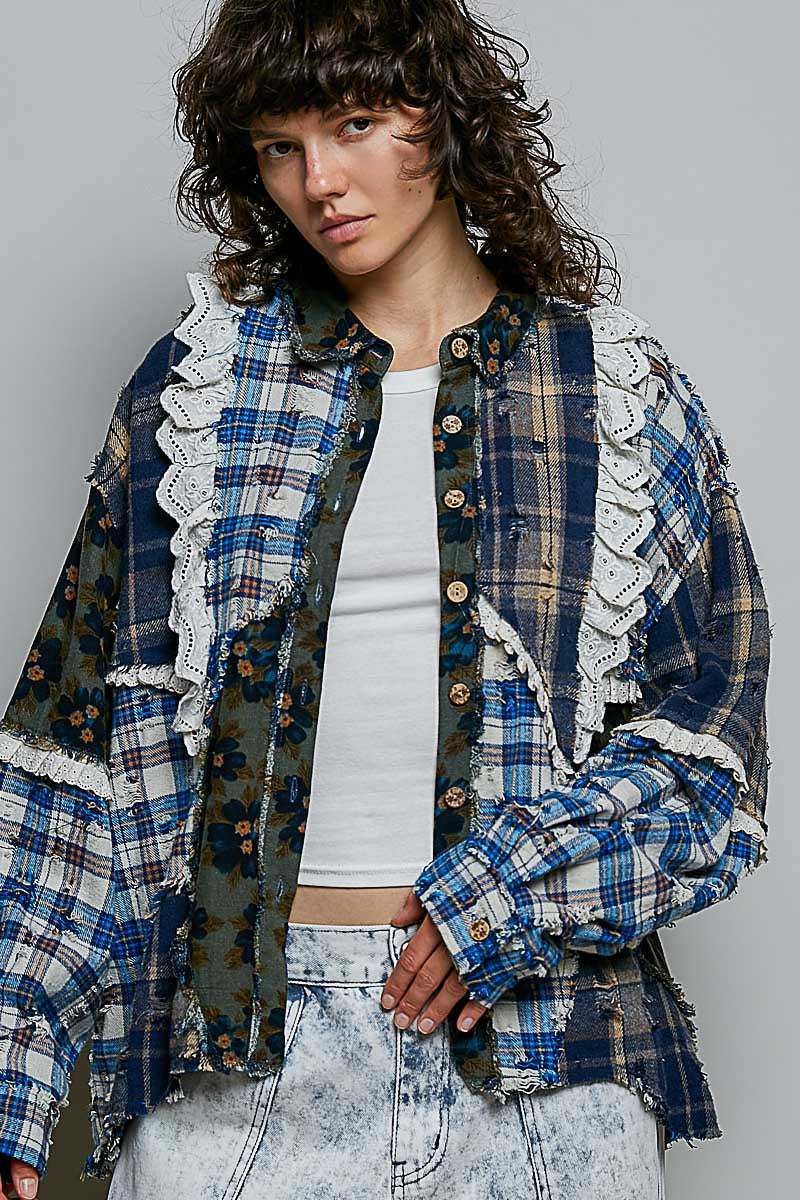 A model wearing a distressed patchwork button-up shirt with blue, green, and brown plaid patterns, white lace trim, and frayed edges, layered over a white crop top and light-wash jeans.