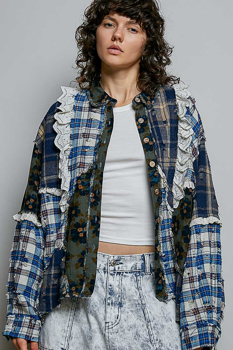A model wearing a blue and white patchwork plaid shirt jacket with white lace ruffles, styled over a white crop top and light-wash denim shorts against a gray studio background.