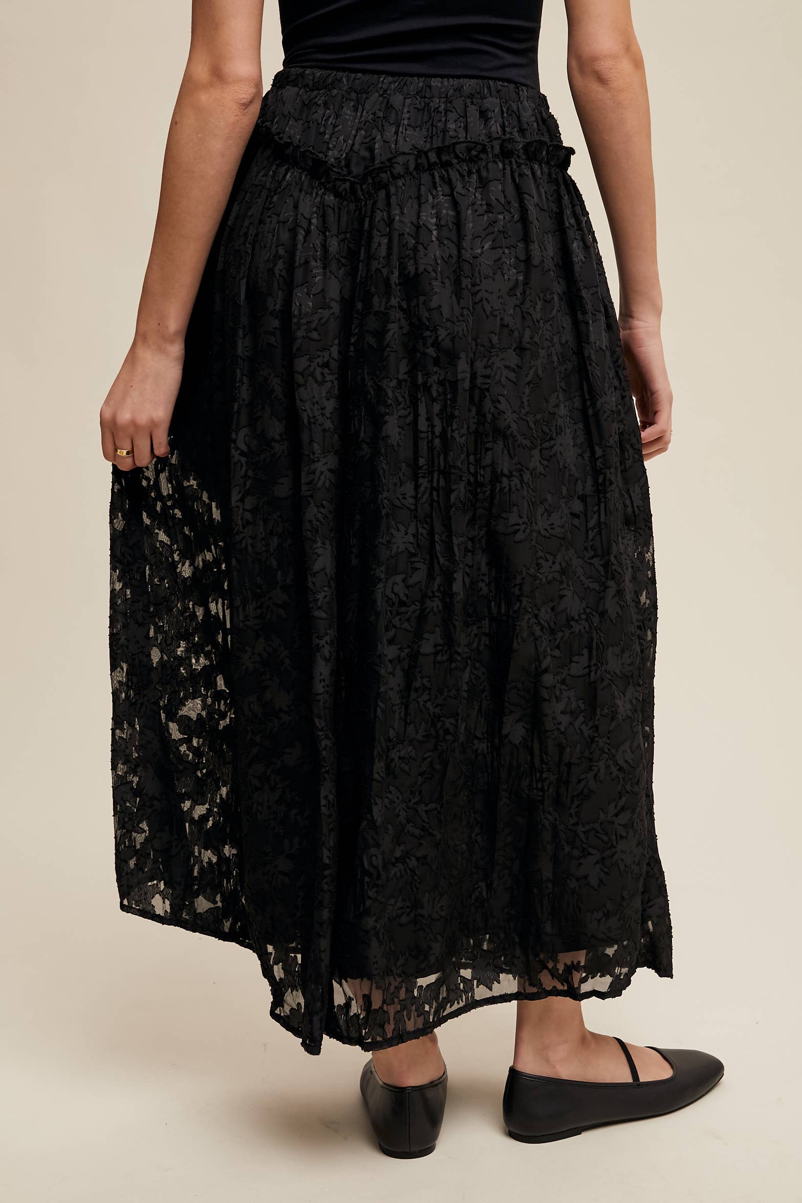Black floral lace maxi skirt with elastic drawstring waist, ruffle trim and pockets; semi-sheer bubble hem, styled with black Mary Jane flats.