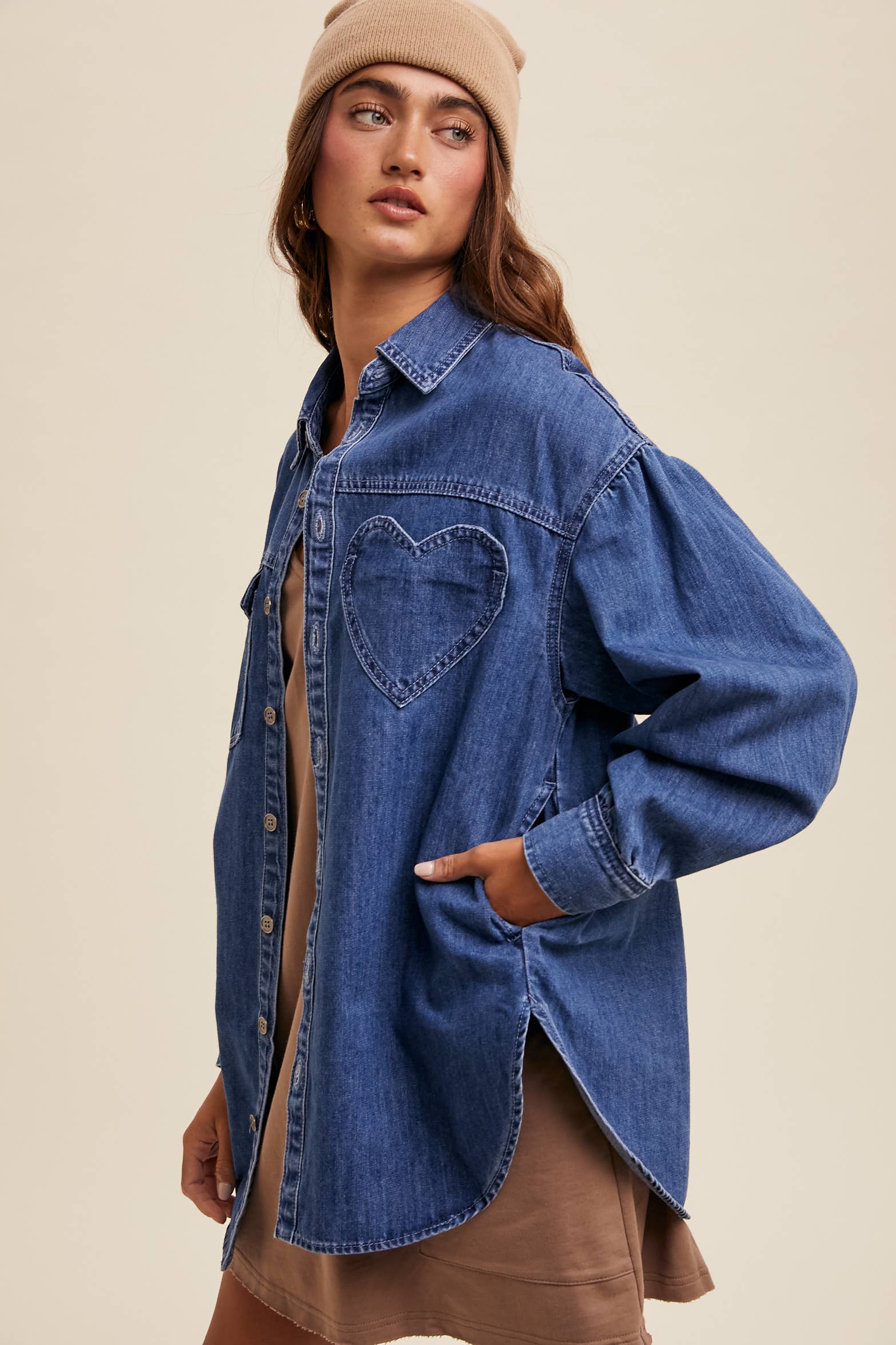 Side view- Medium-wash oversized denim shacket with button front, drop shoulders, balloon sleeves, side pockets, and a curved shirttail hem with side slits.