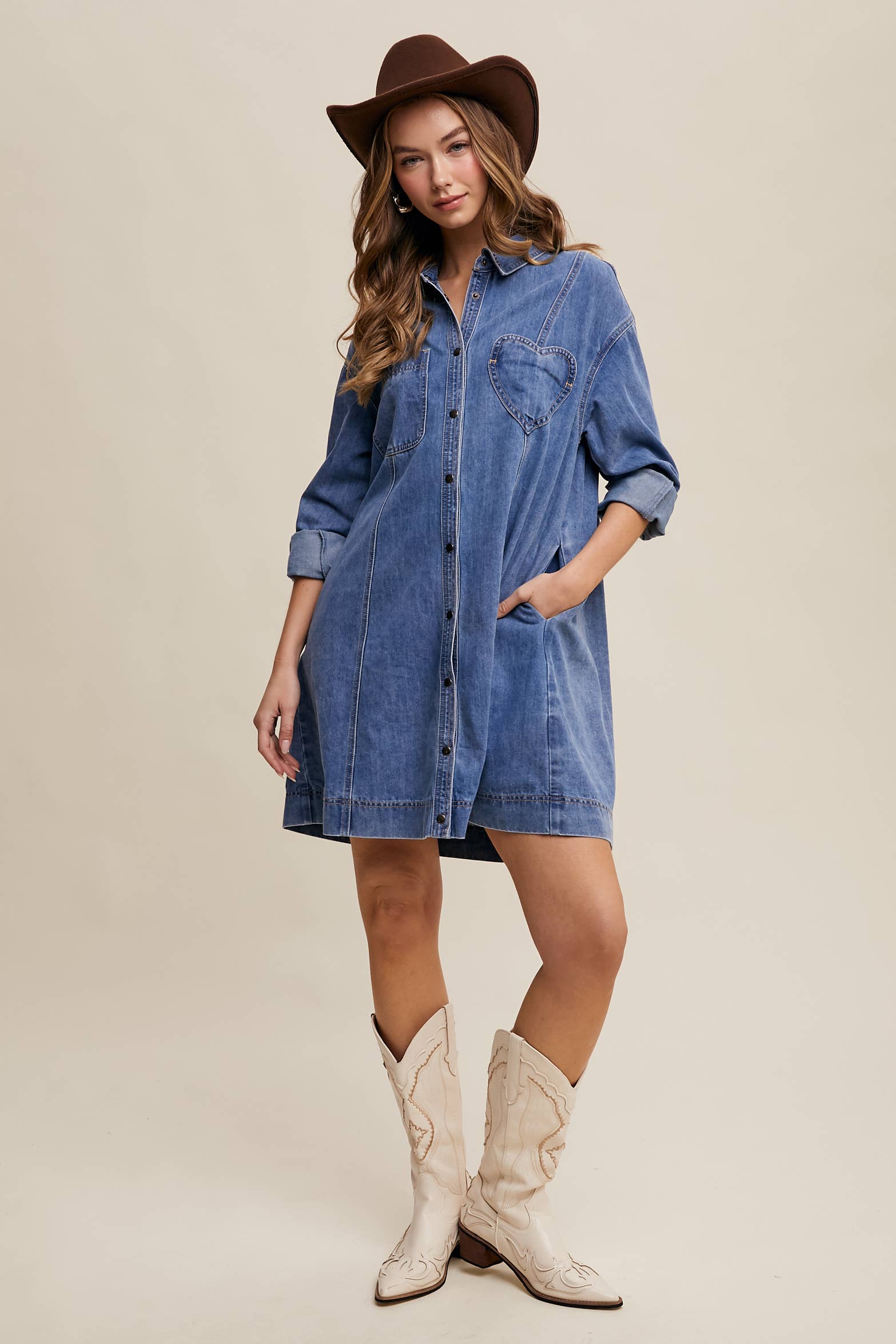 Medium-wash denim shirt dress with snap button front, heart-shaped chest pocket, rolled long sleeves, and a relaxed mini silhouette.