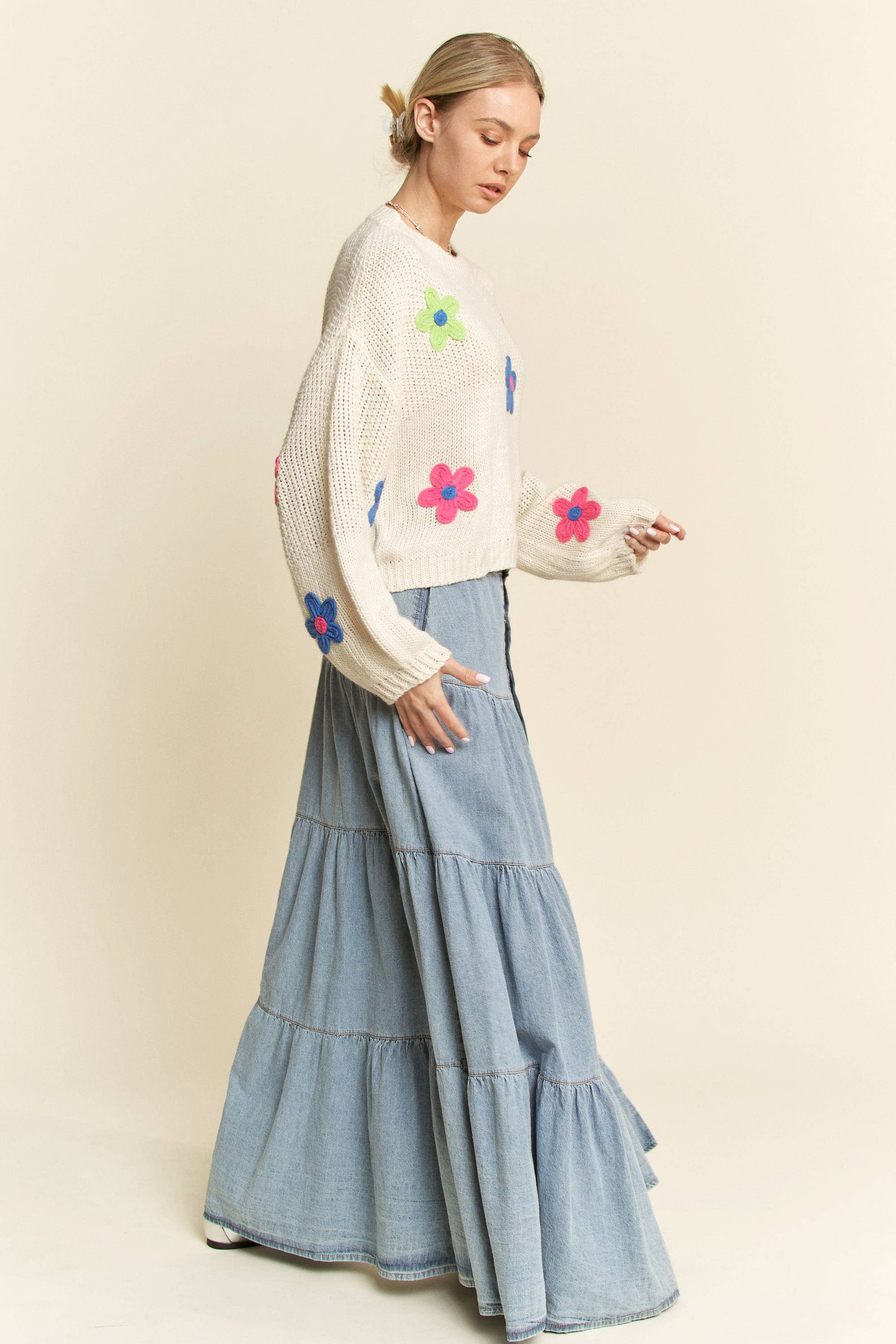Side view- Cream knit sweater with colorful 3D floral appliqués in pink, blue, and green, styled with a button-front light denim skirt.
