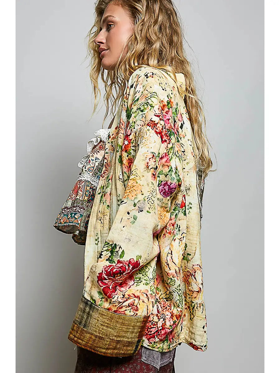 A woman wearing Peace in Bloom Yellow Floral Reversible Boho Jacket bohemian floral print jacket with red, pink, and green flowers, shown from a side profile against a plain gray background.