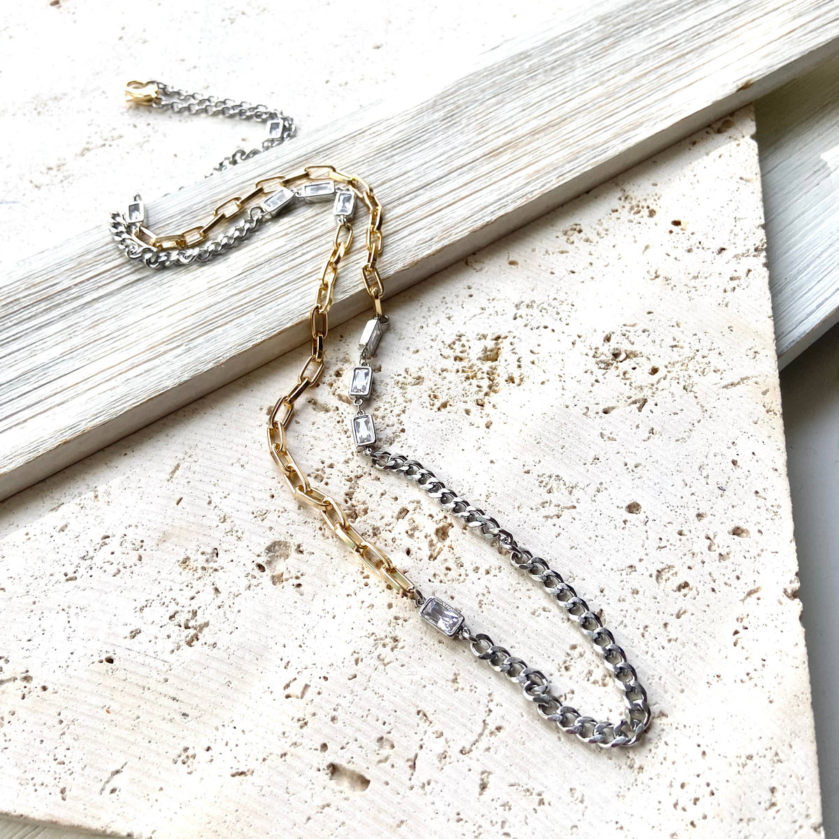 Two necklaces, one gold and one silver, on a textured surface.
