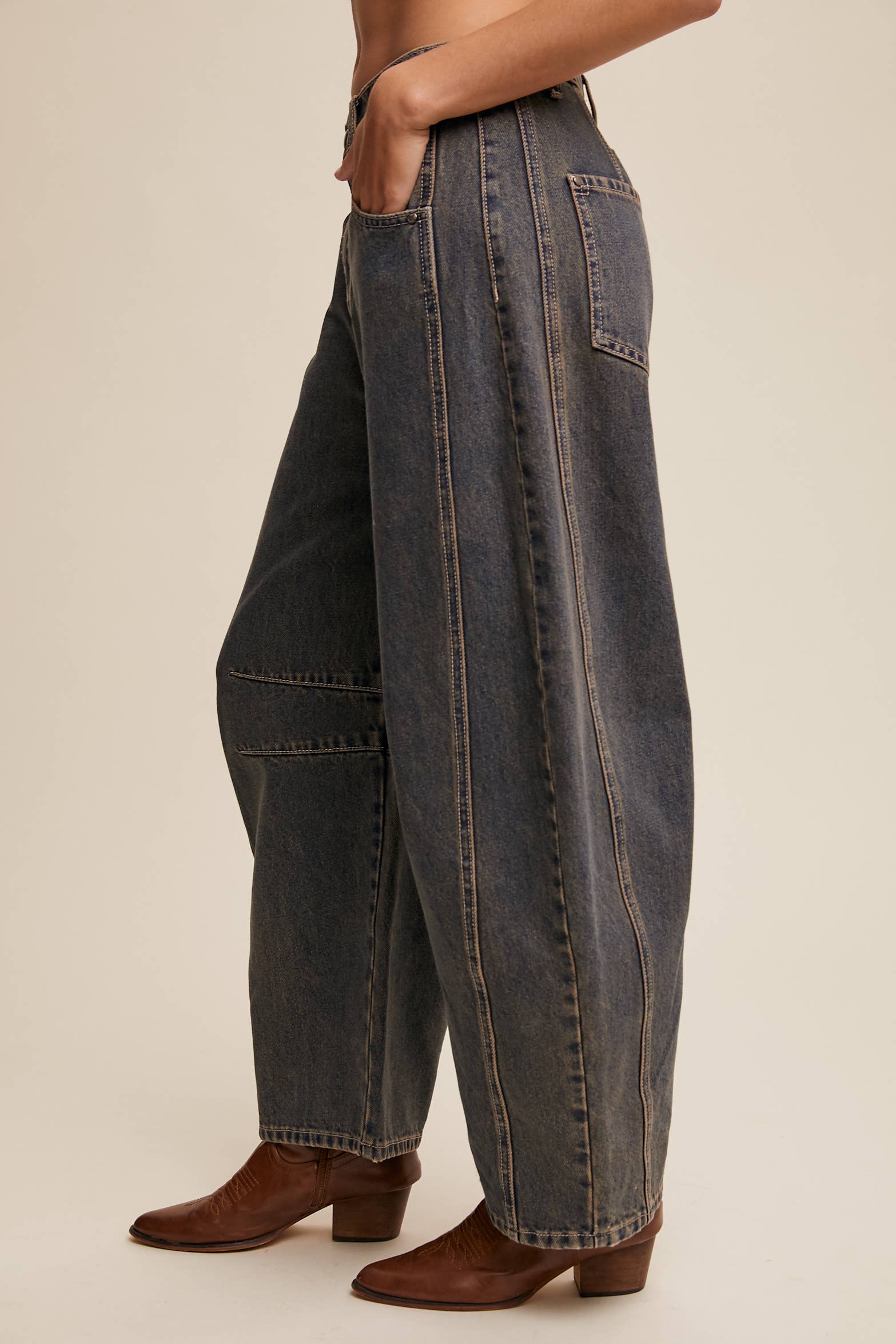 Side view- Dark wash wide-leg jeans with relaxed fit, seam detailing across the knees, and a high-rise waist, styled with brown ankle boots.