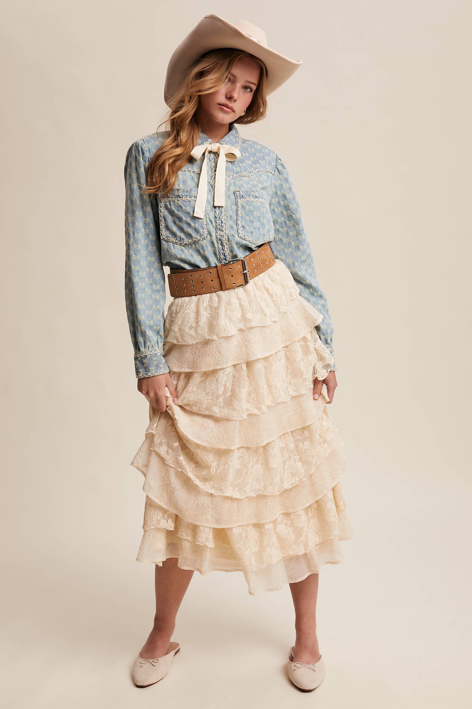 Light-wash denim blouse with cream bow-tie collar, tonal mini-bow pattern, braided contrast stitching, snap front, and two chest pockets.