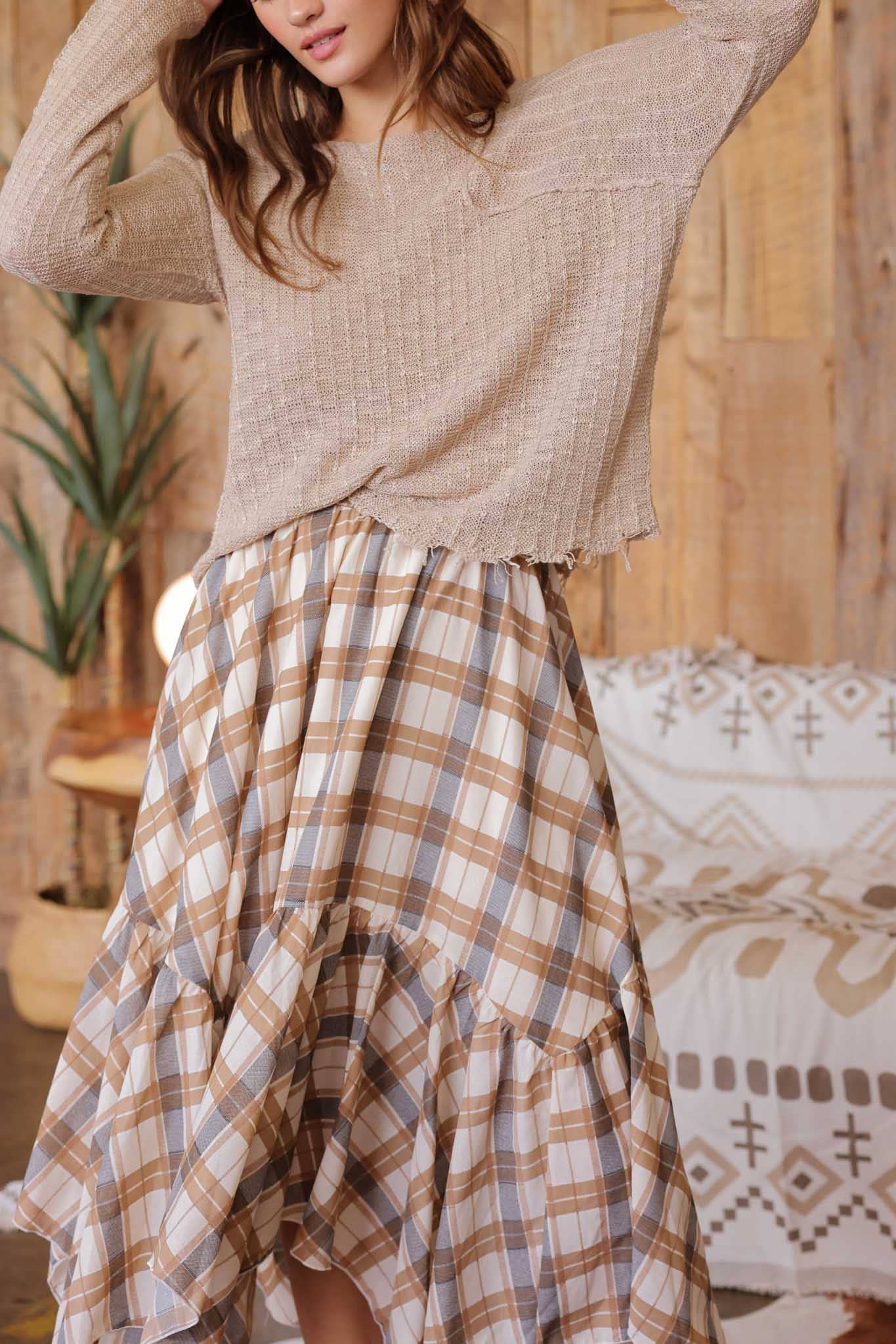 Woman wearing a beige sweater and plaid skirt in a cozy indoor setting.
