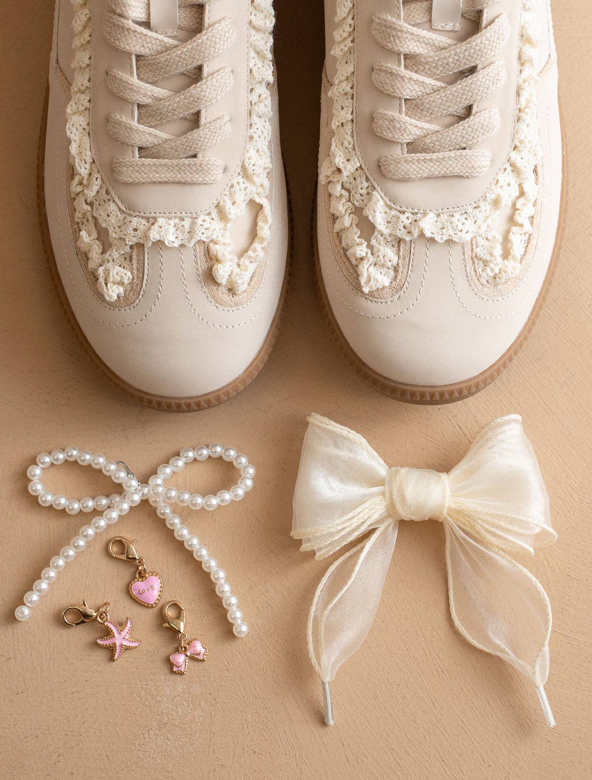 Ivory lace-trim low-top sneakers on model; pearl-beaded laces with gold charms, gum soles, and sheer ribbon laces on the floor, top-down view.