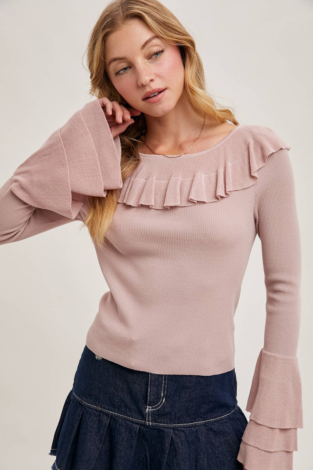 Rose ribbed knit sweater with ruffle neckline and tiered bell sleeves, paired with a dark denim skirt.