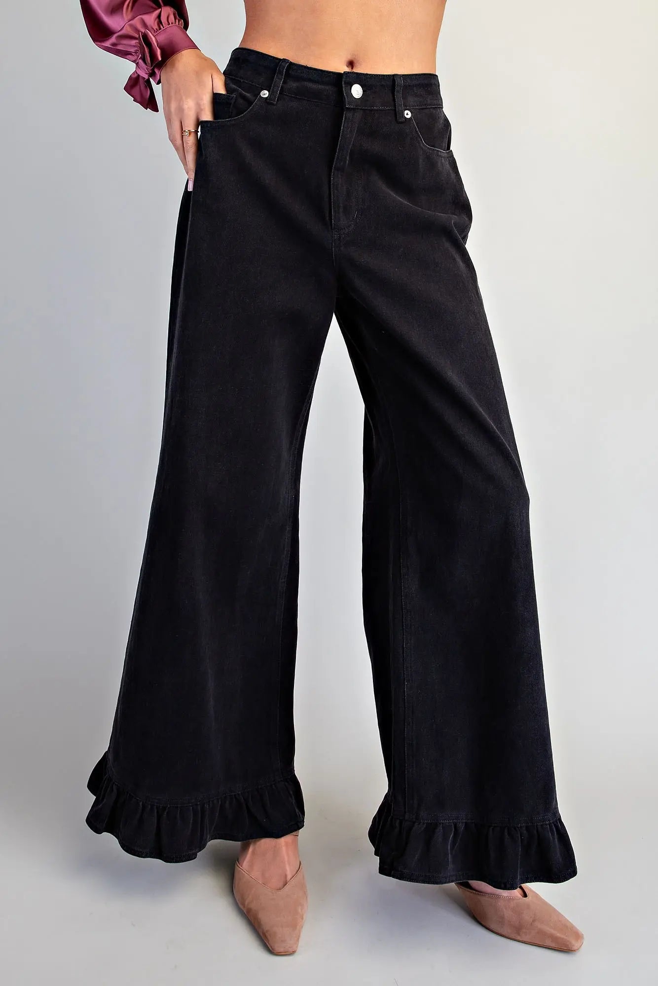Front view of women's black high-rise wide-leg denim pants with silver button closure, front pockets, and ruffled hem, styled with nude pointed-toe flats