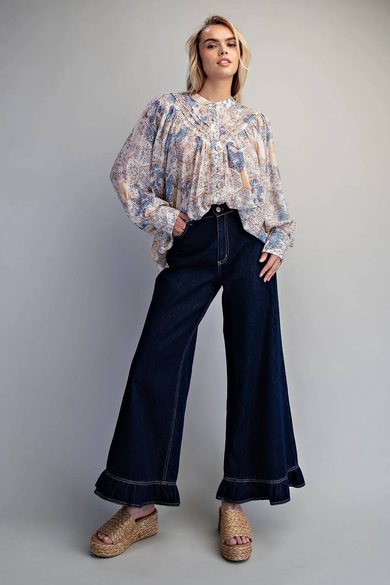 Full-length outfit view of dark wash wide-leg ruffled hem denim pants styled with a floral boho blouse and woven platform wedge sandals