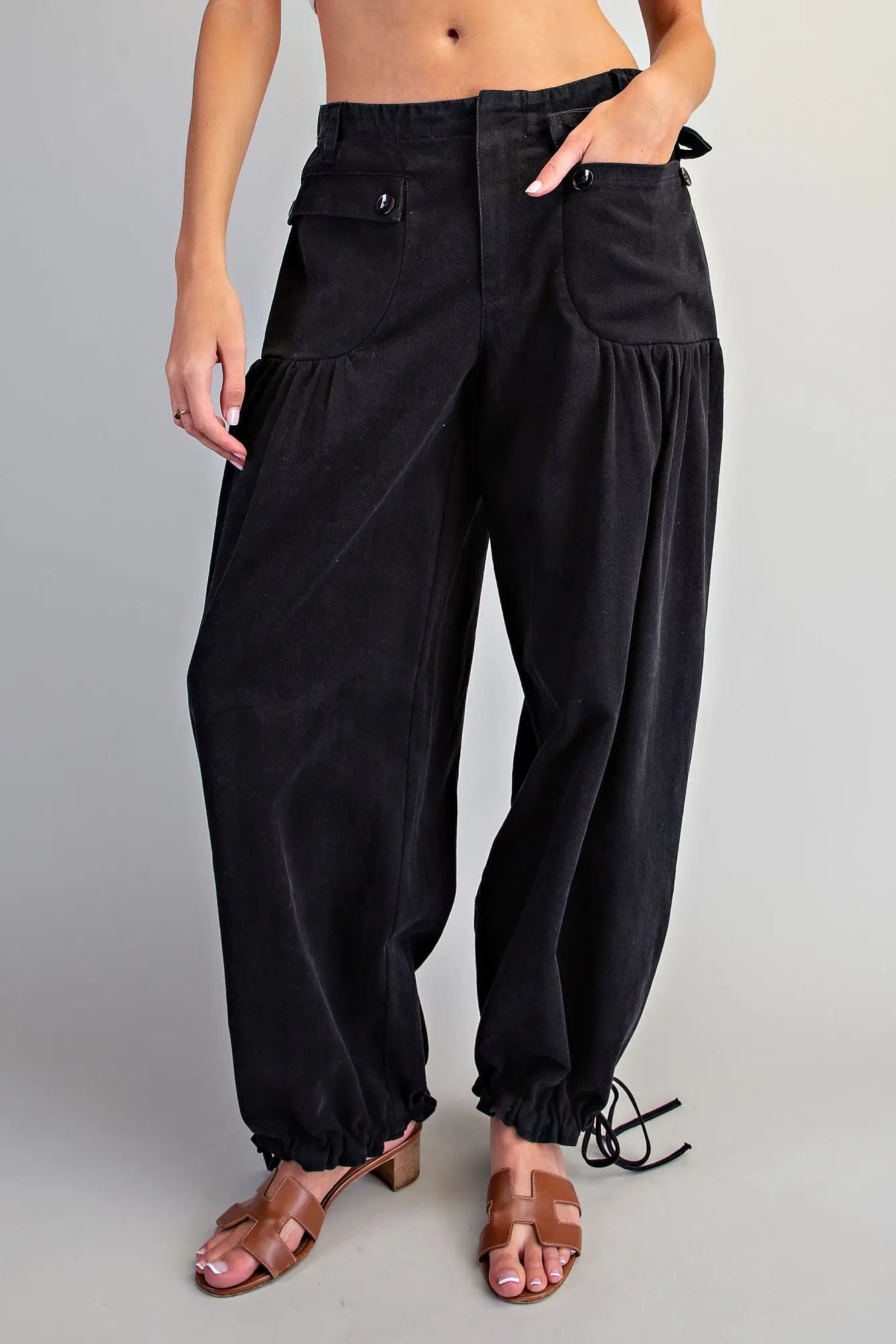 Women's black mineral washed relaxed tie cuff pants — front view showing button pocket detail, gathered leg, and drawstring ankle ties, styled with heeled sandals