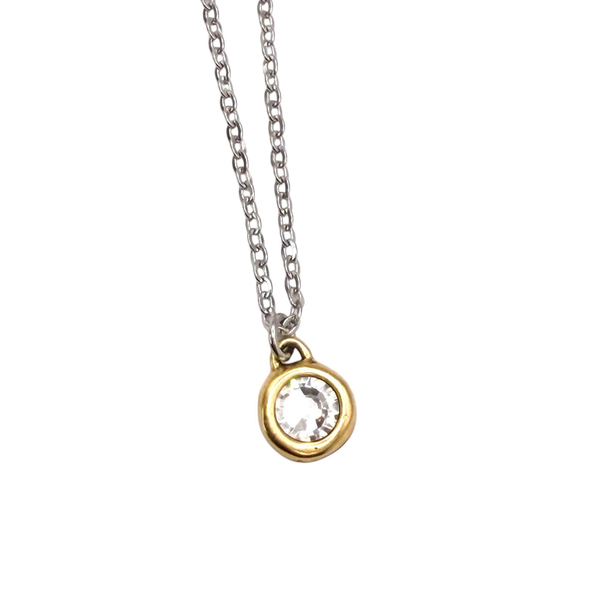 A delicate silver chain necklace featuring a small gold bezel-set pendant with a clear round gemstone, shown against a plain white background.