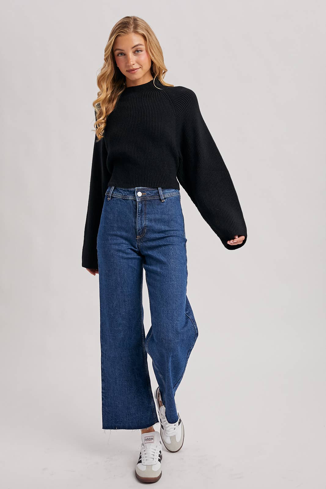 Black ribbed mock-neck sweater with long wide sleeves and a cropped fit, styled with high-rise blue jeans.