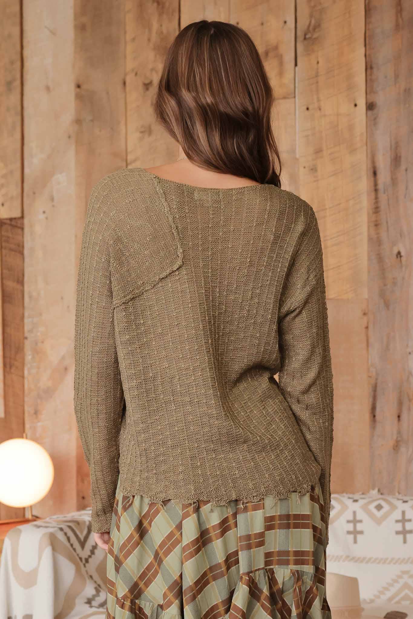 Back view of model wearing olive distressed lightweight sweater featuring ribbed knit texture and raw edge hem, paired with plaid ruffle skirt