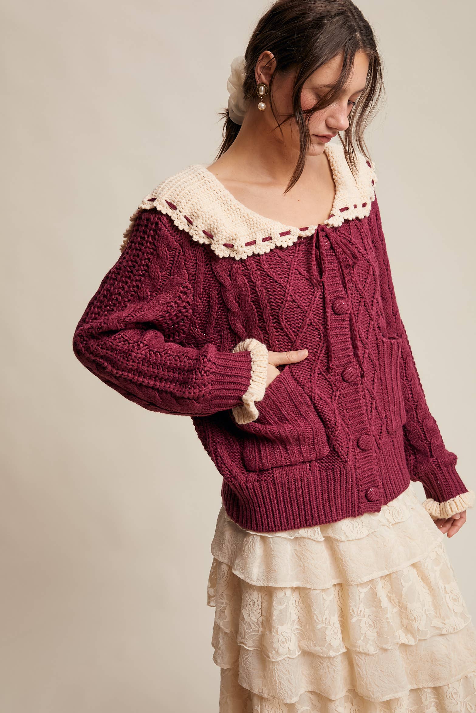 Woman wearing a burgundy cardigan with lace trim on a plain background