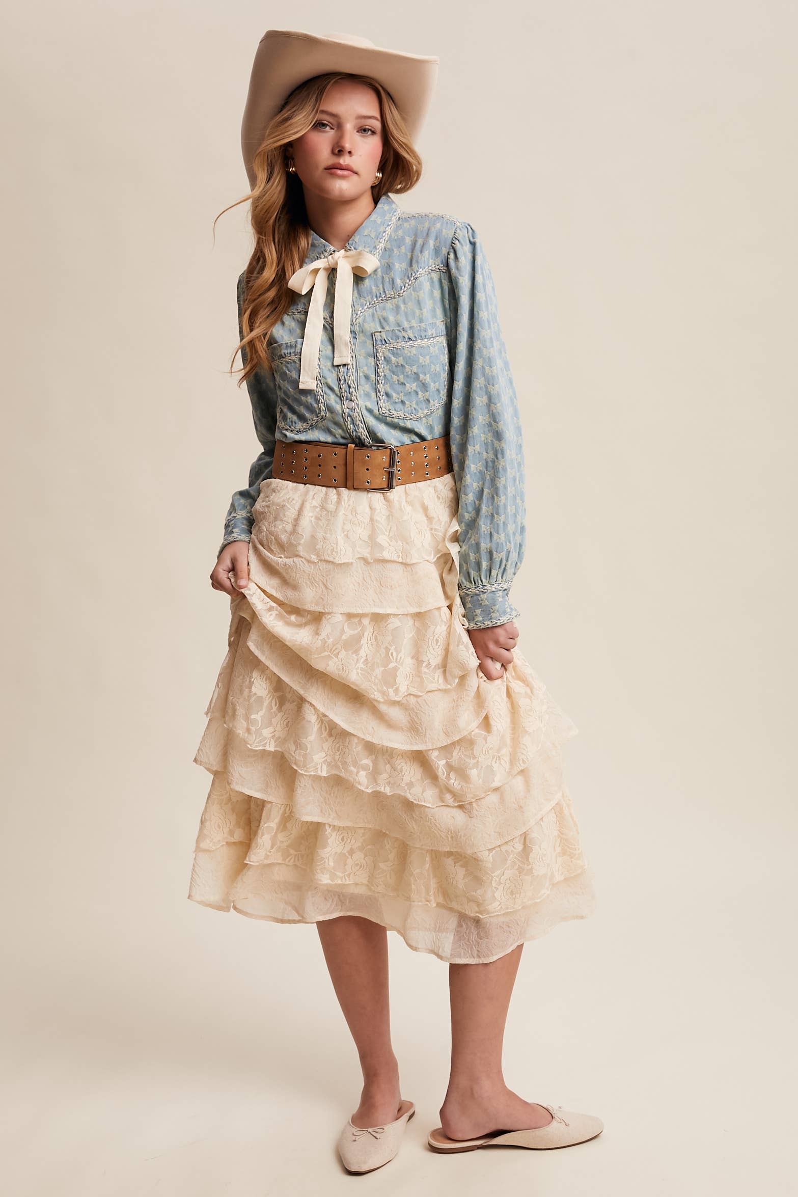 Light-wash denim blouse with cream bow-tie collar, tonal mini-bow pattern, braided contrast stitching, snap front, and two chest pockets.