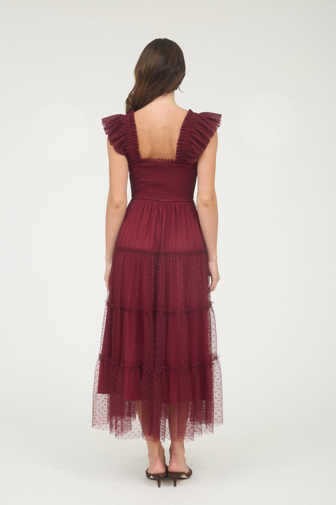 Back view of Model wearing burgundy smocked midi dress with ruffle sleeves, tiered dotted mesh overlay, and flowy A-line silhouette.