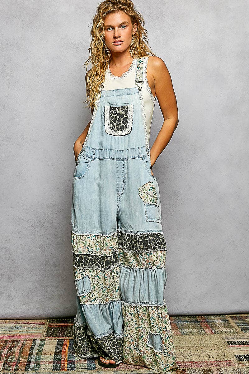 Model wearing mixed print ruffle wide leg overall in denim — front view, leopard print bib pocket with lace trim, tiered floral and animal print ruffle legs, relaxed fit