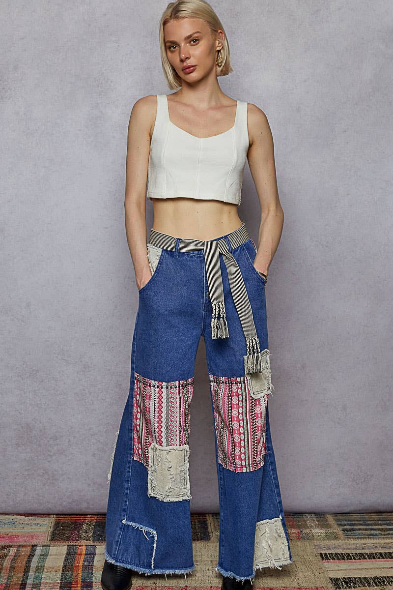 black and cream striped woven belt with braided fringe tassels tied at the waist of blue denim jeans.