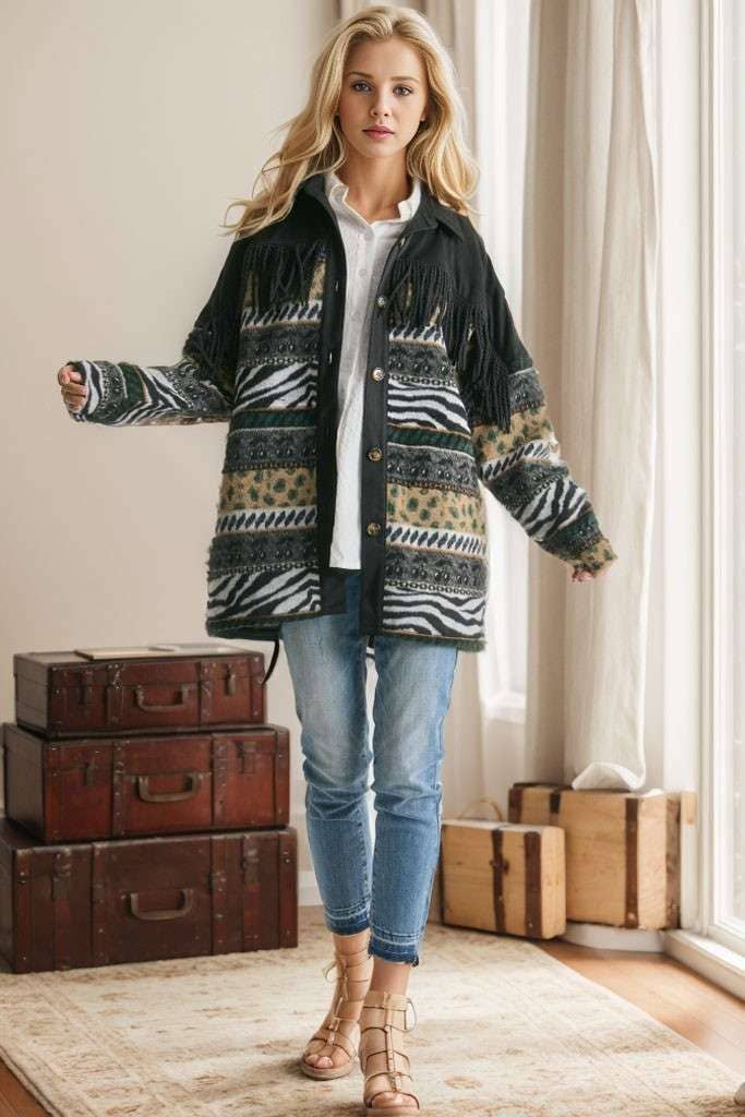 Brown Aztec print shacket with fringe detail, button closure, and patterned sleeves, styled with cream pleated pants while seated on a sofa.