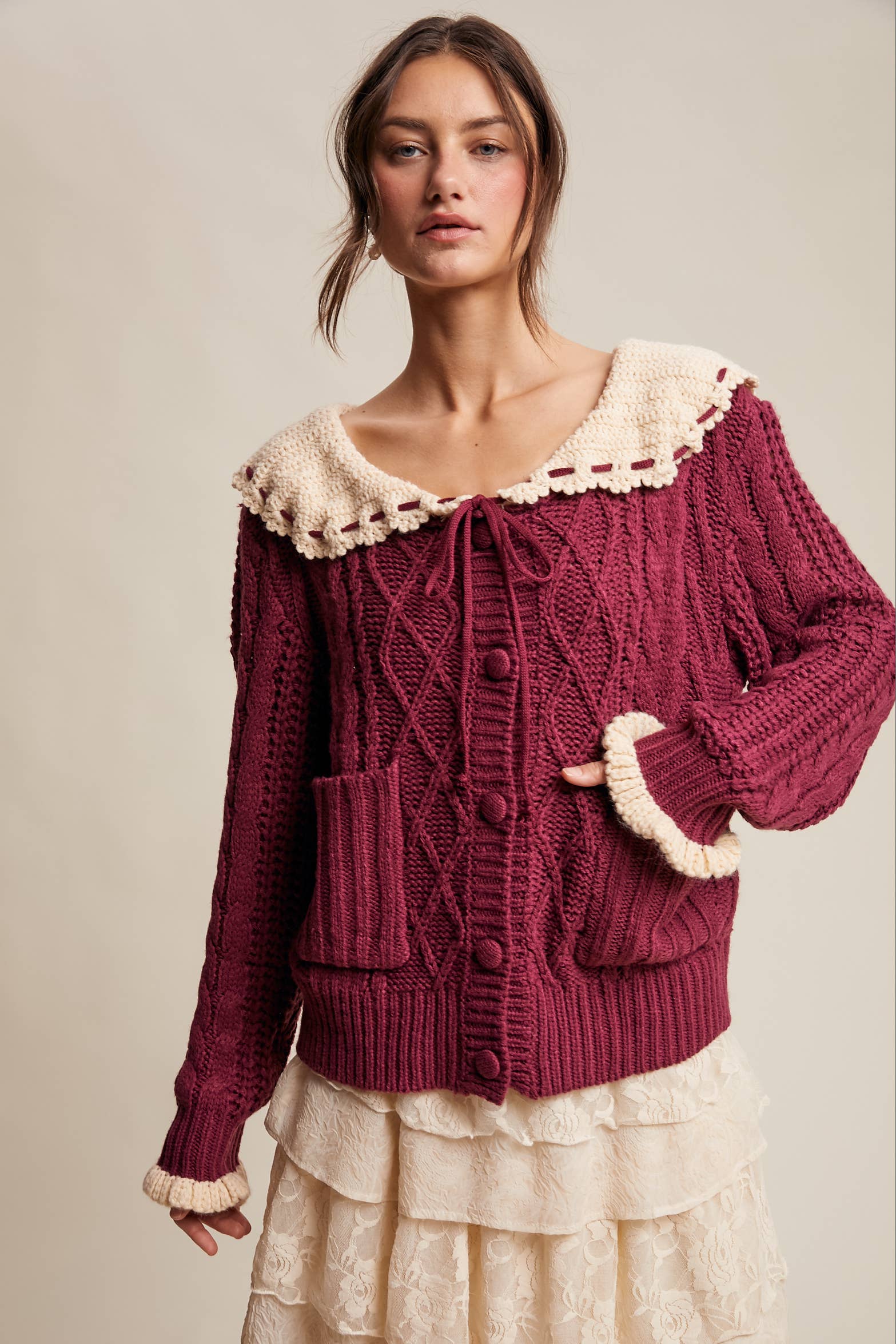 Woman wearing a burgundy knitted cardigan with lace trim on a beige background