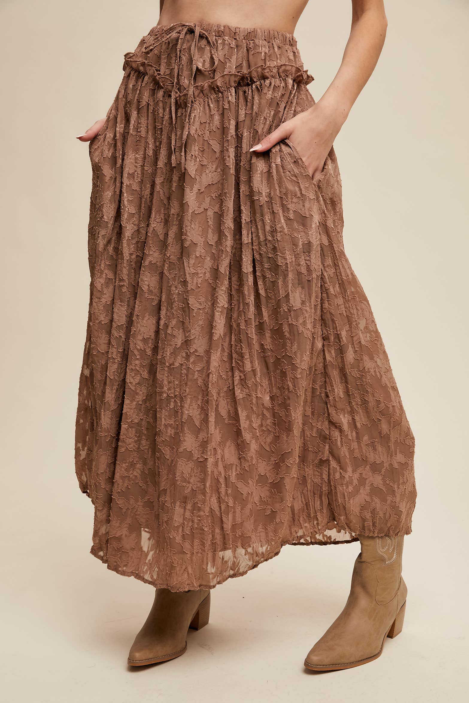 Mocha brown floral lace maxi skirt with elastic drawstring waist, ruffle trim, and side pockets; billowy bubble hem, styled with tan western boots.