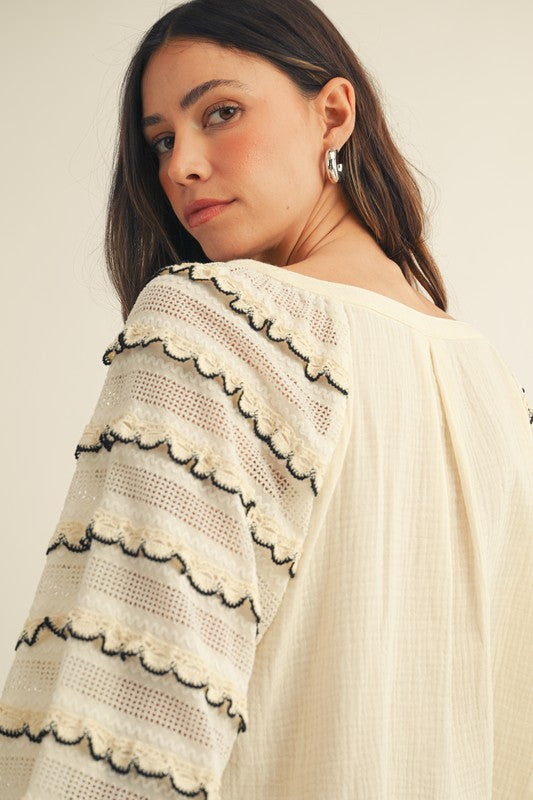 Close-up back view of cream gauze blouse with sheer lace sleeves, scalloped ruffle rows and black trim.