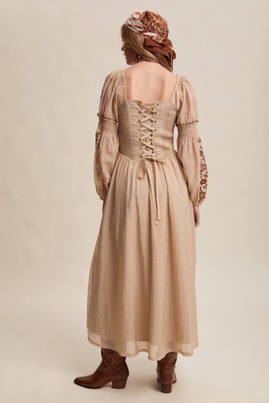 Back view of beige boho maxi dress with lace-up corset back, smocked bodice, and embroidered long puff sleeves.