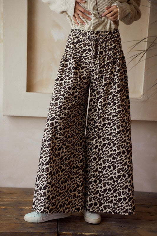Front view — leopard print wide-leg pants with high rise and tie waist, flowy woven drape; styled with a beige knit sweater on model.