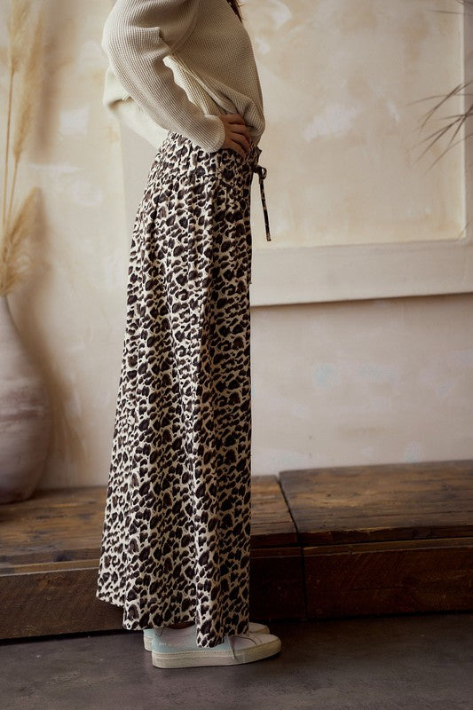 Side view — leopard print wide-leg pants with high-rise elastic waist and tie belt, flowy drape, ankle length on model.