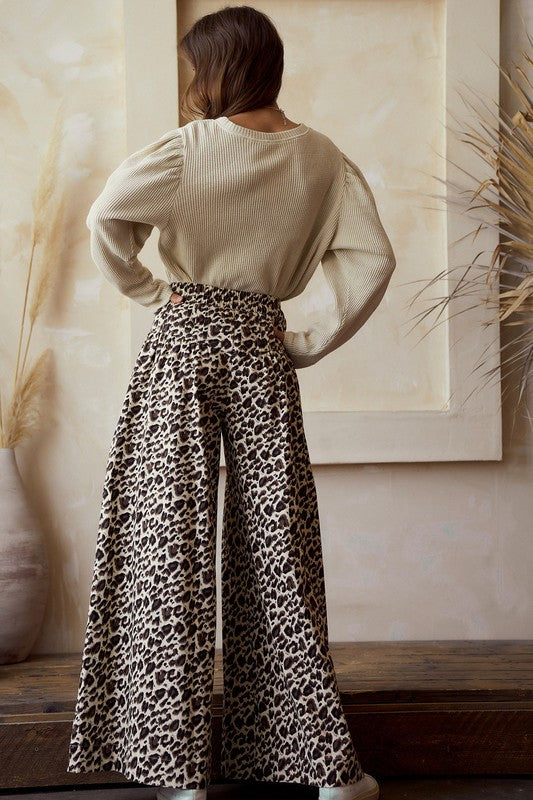 Back view — leopard print wide-leg pants with high-rise smocked elastic waist and flowy drape, full length on model.