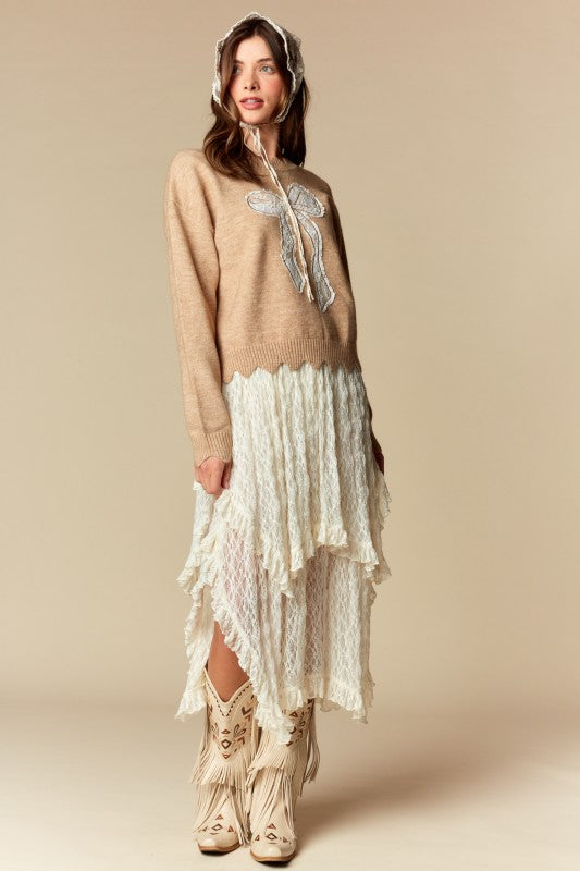 Camel knit sweater with white lace bow applique, relaxed fit, ribbed cuffs and scalloped hem, three-quarter front view on model.