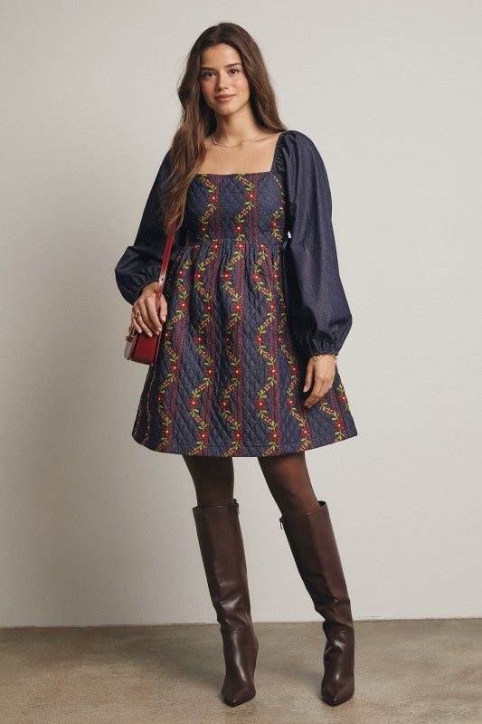 Model in a navy quilted dress with colorful floral embroidery and corset-laced waist, denim puff sleeves; side view, knee-length.