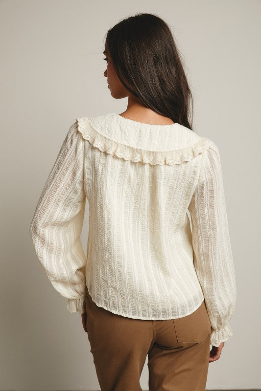 Back view of ivory textured blouse with ruffled collar detail and long sleeves.