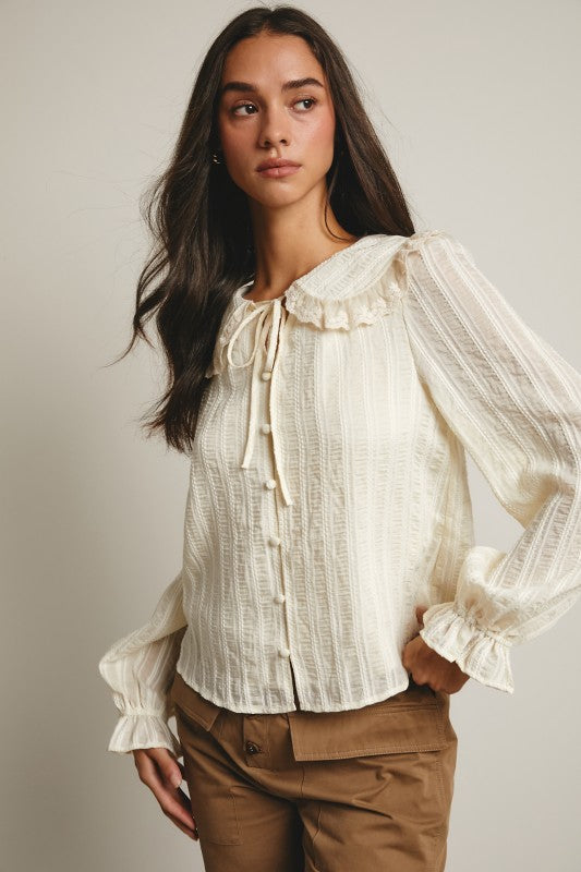 Ivory tie-neck blouse with ruffled Peter Pan collar, covered buttons, textured stripe fabric, and long puff sleeves.