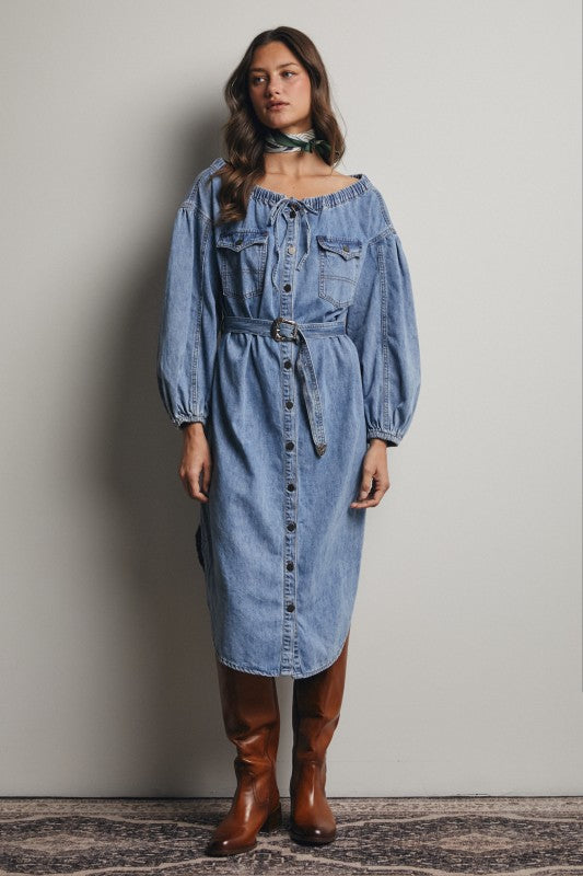 Woman wearing a denim dress with brown boots against a plain background