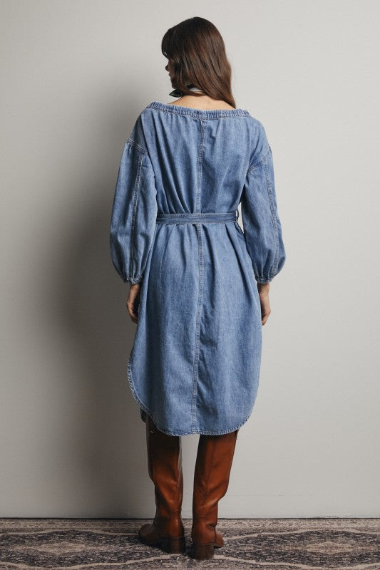 Woman wearing a blue denim dress with brown boots against a plain background