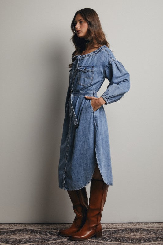 Woman wearing a blue denim dress with brown boots against a plain background