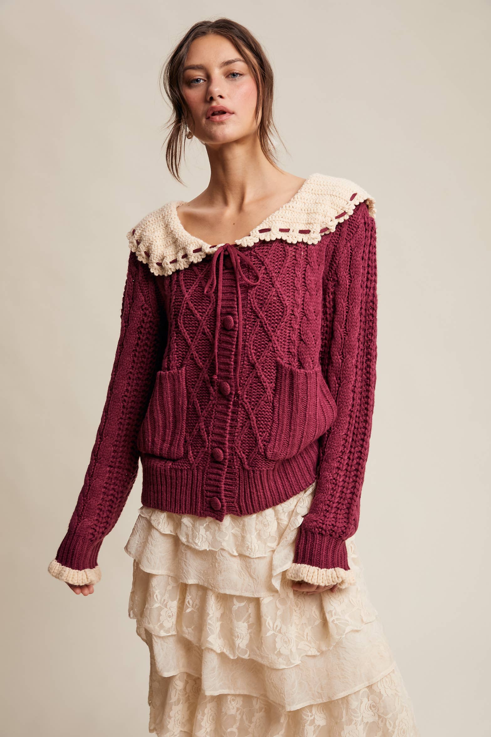 Woman wearing a burgundy knitted sweater with lace trim on a beige background