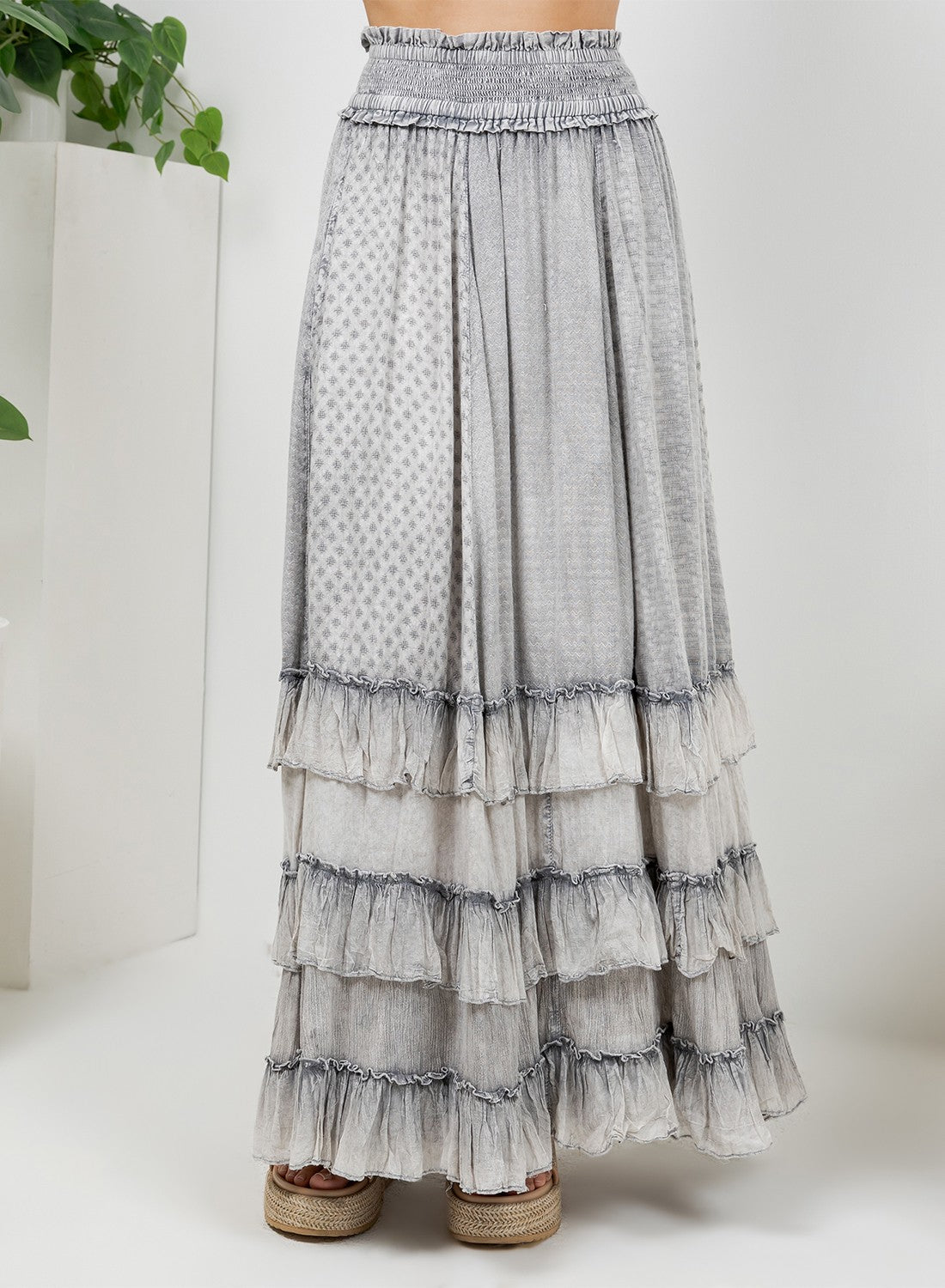 A long tiered maxi skirt in a light gray and white patterned fabric, shown on a model wearing brown espadrille wedge sandals against a white studio background.