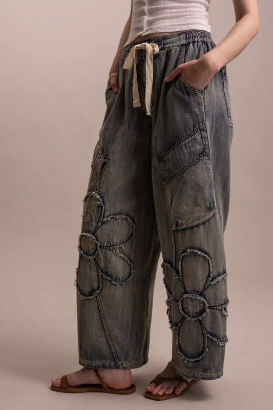 Close-up of oversized raw-edge daisy patchwork on wide leg denim cargo pants with drawstring waist