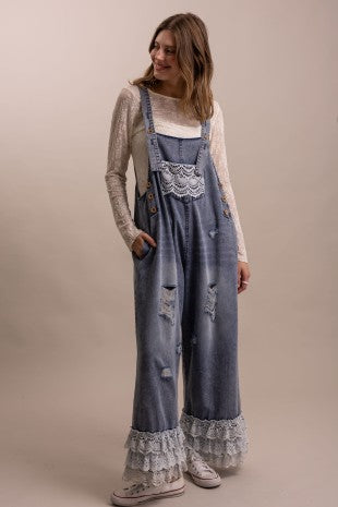 Full length front view of distressed denim overall with crochet lace bib pocket, wide leg silhouette, and tiered lace ruffle hem