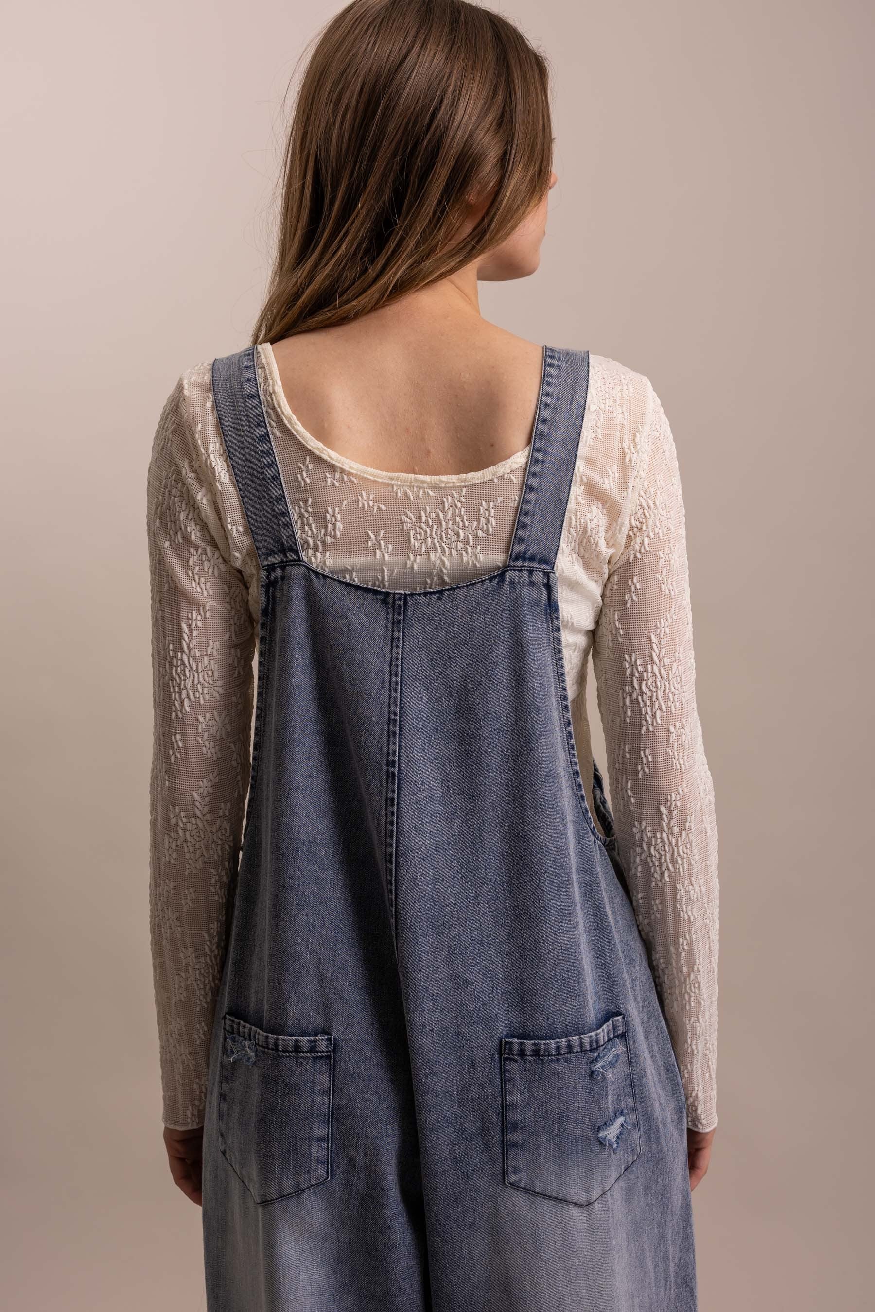 Close up Back view of distressed wide leg denim overall with tiered lace ruffle hem and adjustable straps, two back pockets