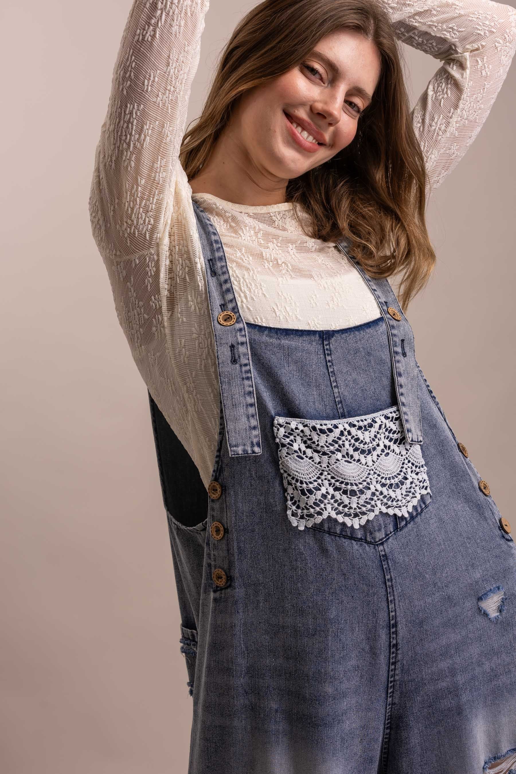 Close-up of crochet lace bib pocket on distressed denim overall with button strap hardware and side button closures