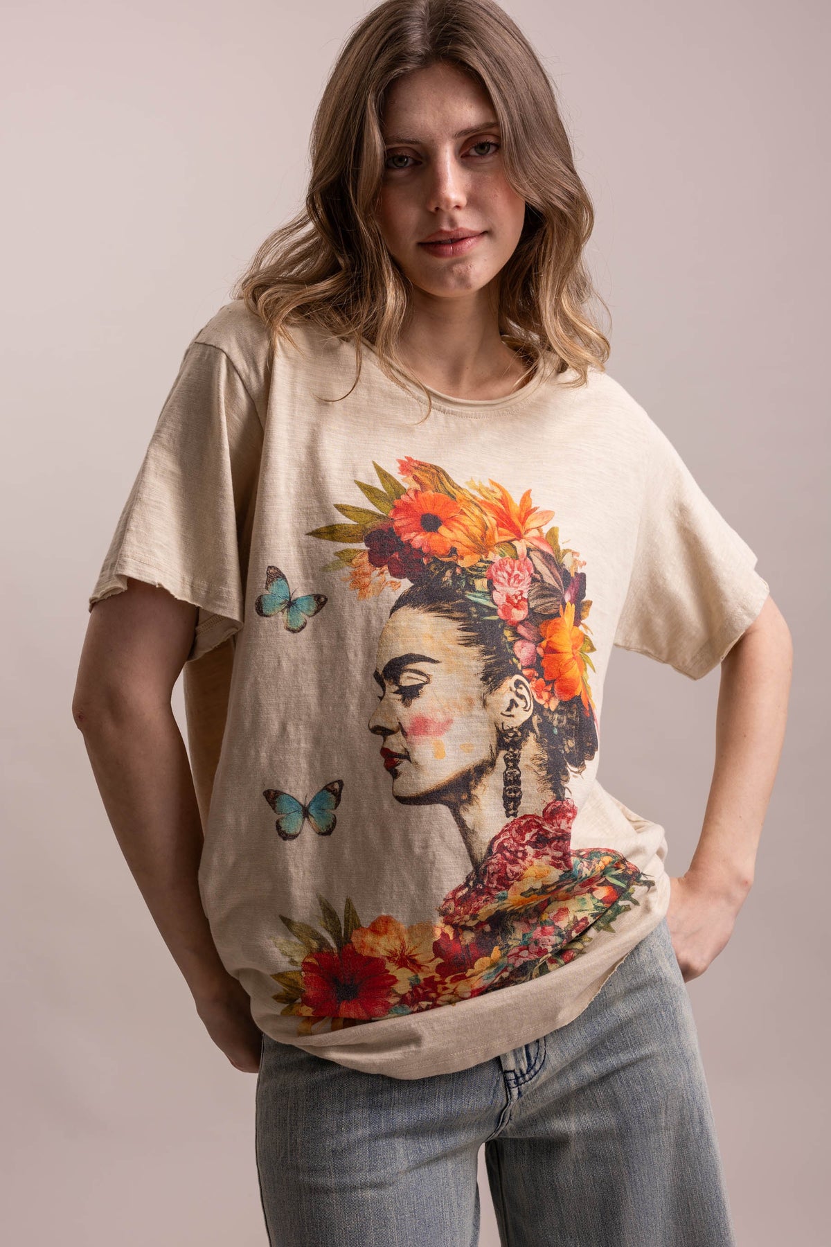 Woman wearing a beige t-shirt with a Frida Kahlo graphic design on a plain background
