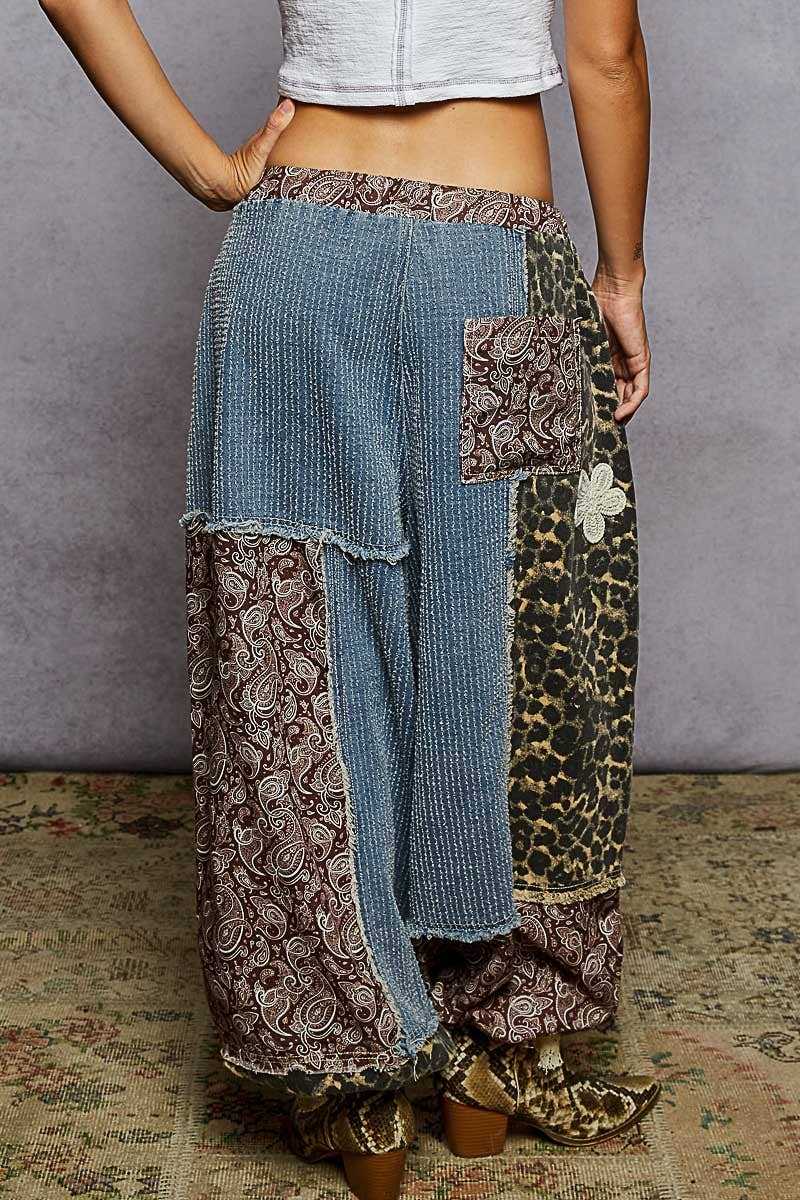 Person wearing patchwork pants with floral and leopard print patterns on a textured floor.