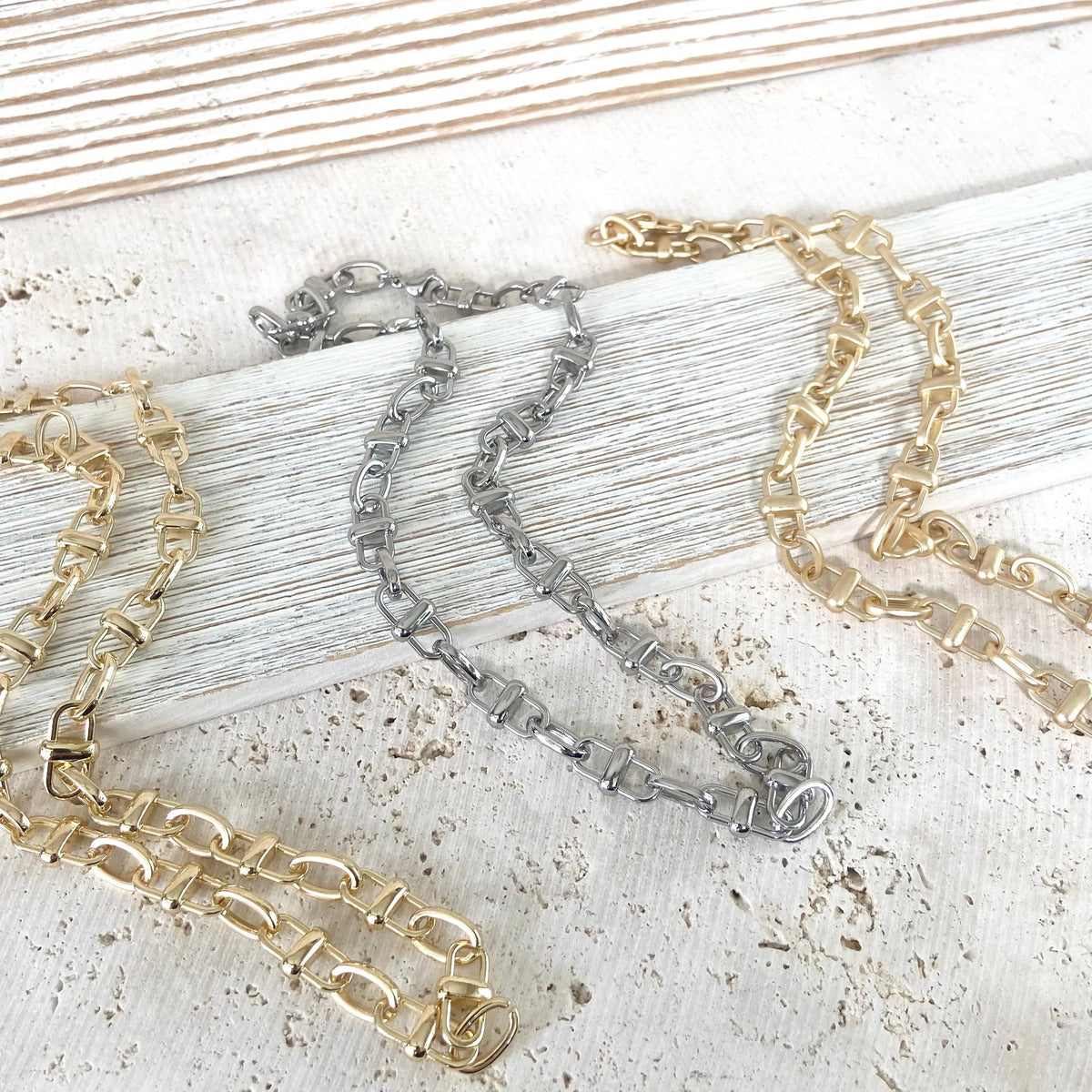 Three chain necklaces in gold, silver, and rose gold on a textured surface.